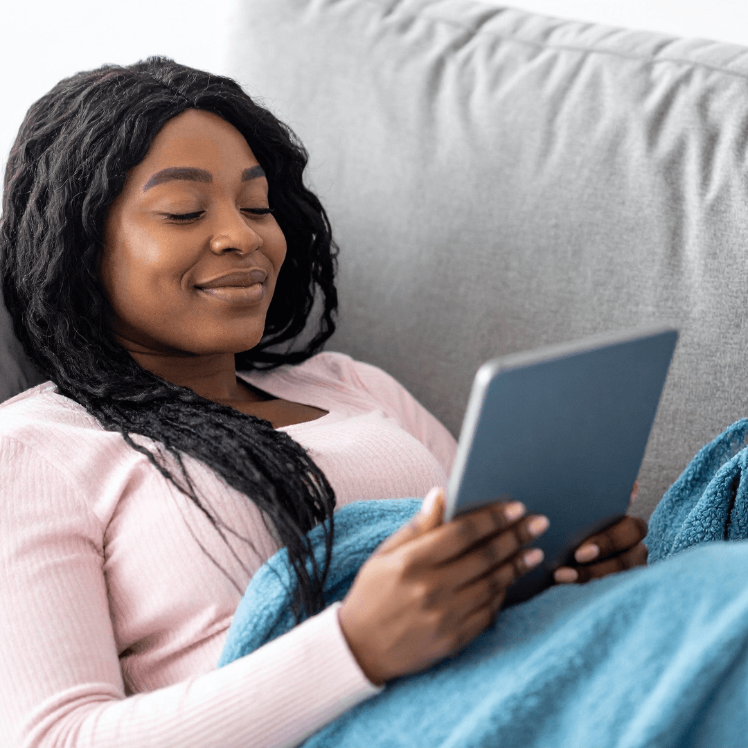 Frau liest entspannt mit dem Tablet auf dem Sofa
